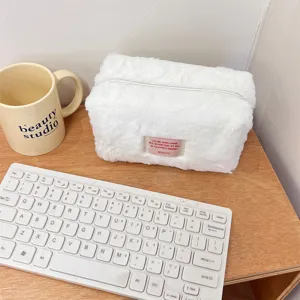 Detailed view of the soft white plush cosmetic bag, cozy texture and neat desktop scene.