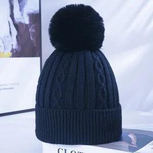 Black cable knit beanie detail showing thick texture and large fluffy faux fur pom-pom.