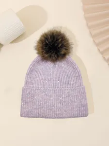 Close-up detail of winter warm knitted beanie hat with faux fur pom-pom and sparkling sequin.