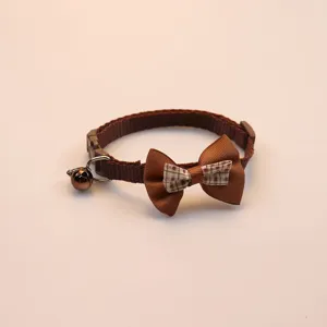 Close up of brown pet collar detail, featuring cute plaid bowknot and small bell accessory.