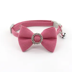 Close-up detail of pink pet cat dog collar with fabric bow, rhinestone ring, and metal bell.