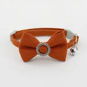 Orange pet collar detail showcasing rhinestone bowknot embellishment and silver bell pendant closeup