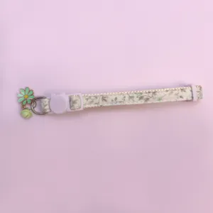 Close-up detail view of the floral pet collar featuring a cute cat buckle and a green bell pendant.