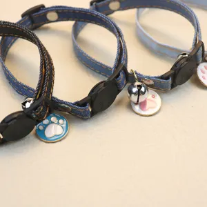 Close-up detail of denim pet collar with cute bell and colorful paw pendant, adjustable design.