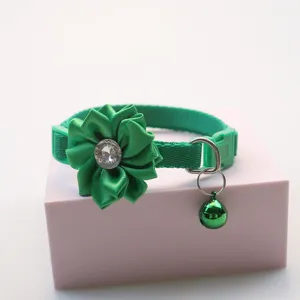 Detail shot of a green pet collar featuring a fabric flower, rhinestone, and bell.