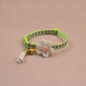 Close-up detail of green pet collar featuring white knitted flower, bell and tassel.