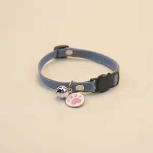 Close-up detail of blue denim pet collar featuring a silver bell and pink paw print pendant.