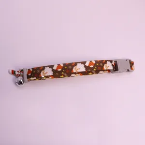 Détail du collier de noël pour animaux, sangle marron motif père noël, clochette et pendentif.