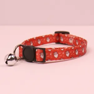 Close-up detail of red Christmas pet collar with Santa pattern, plastic buckle, and bell.
