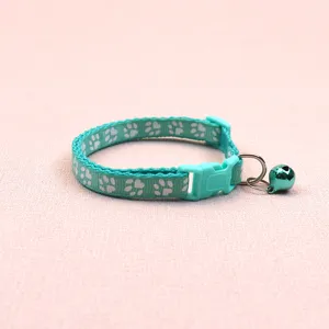 Turquoise pet collar detail featuring white paw print pattern, plastic buckle and bell.