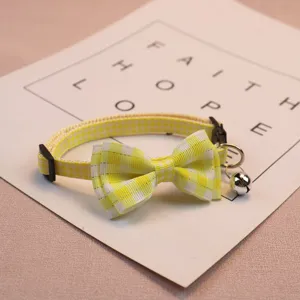 Close-up detail of yellow plaid pet collar featuring cute bow and metal bell for small pets.