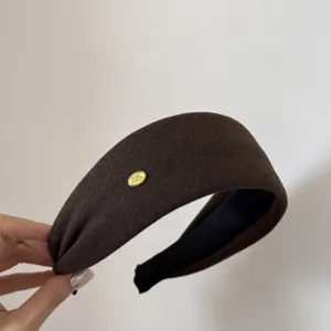 Vista detallada de la diadema ancha marrón con una elegante etiqueta de marca de metal dorado.