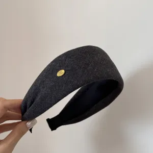 Detalle de una diadema de tela ancha gris oscura con un elegante adorno de metal dorado.