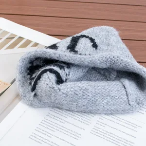 Primer plano detallado del gorro de punto gris con motivo de letras negras en madera.