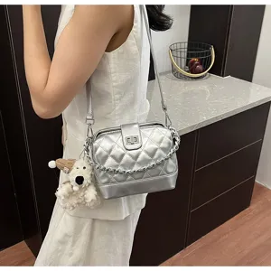 Dettaglio di una borsa a tracolla argentata trapuntata con catena e ciondolo di peluche.