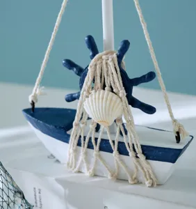Wooden sailboat model detail showing decorative net, ship wheel and seashell on desktop.