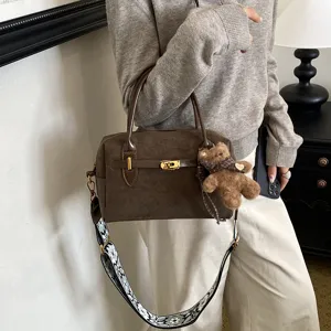 Braune Wildleder Boston Tasche Detail mit Metall Drehverschluss, breitem Gurt und Bärenanhänger.