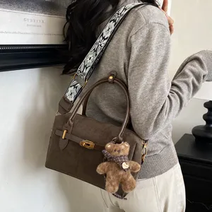 Detailansicht der braunen Wildleder Boston Tasche mit breitem gesticktem Gurt und Bärenanhänger.