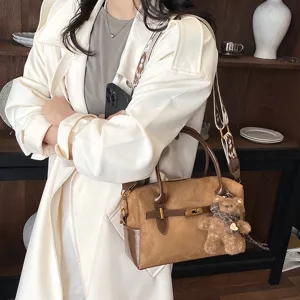Braune Wildleder Boston Tasche Detail mit schicken Schulterriemen und süßem Bärenanhänger.