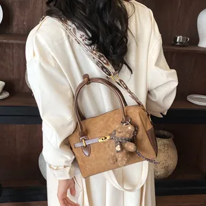 Elegante braune Boston Umhängetasche für Damen mit breitem Riemen und süßem Bärenanhänger.
