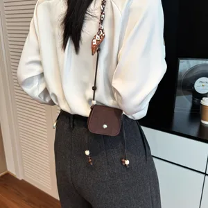 Exquisite mini crossbody bag detail view, stylish brown mini bag with chic scarf strap and beads.