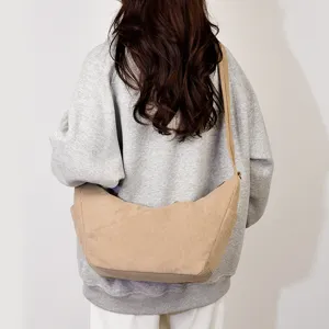 Gedetailleerd uitzicht van een beige corduroy crossbody tas met een zacht en ruim ontwerp gedragen.