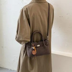 Brown suede crossbody bag with metal turn-lock and chic wooden bead pendant decoration.