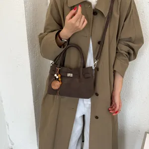 Brown suede handbag detail view, featuring metallic lock closure and charm pendant.