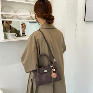 Detail shot of a stylish brown suede crossbody bag with turn-lock closure and chic pendant.