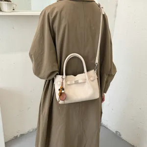 Beige leather shoulder bag detail, elegant crossbody bag with metal turn lock and chic charm.