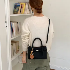 Detail view of black leather shoulder bag with metal turn-lock and wooden charm pendant.