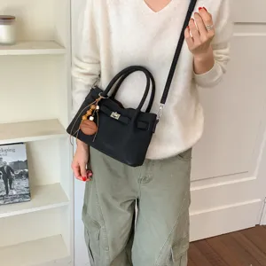 Detail view of stylish black shoulder bag with metal lock closure and cute wooden charm pendant.