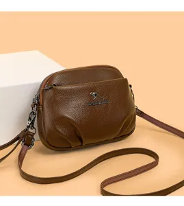 Détail de sac bandoulière en cuir marron, texture souple, logo en métal et sangle réglable.