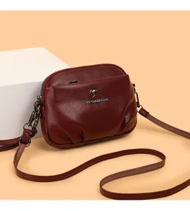 Gros plan d'un sac bandoulière souple rouge vin avec logo kangourou en métal et sangle fine.