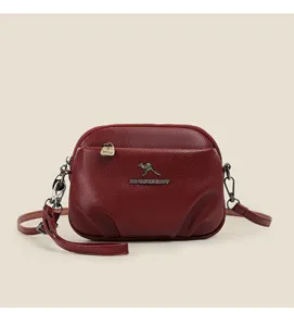 Gros plan d'un sac bandoulière en cuir rouge vin, poches multiples et fermetures métalliques.