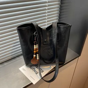 Vista detallada del bolso tote de cuero negro con dije de cuentas de madera para estilo diario.