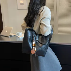 Detalle del bolso tote de cuero negro con colgante de cuentas de madera, estilo informal.