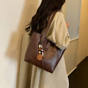Detalle del bolso tote de cuero marron con gran capacidad y colgante de cuentas de madera.