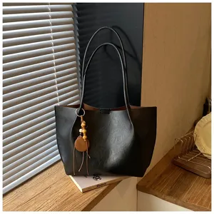 Vista detallada de un bolso tote negro minimalista con asas dobles y colgante elegante.