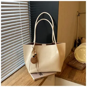 Detalle de cerca del bolso shopper minimalista de piel sintética beige con abalorio.