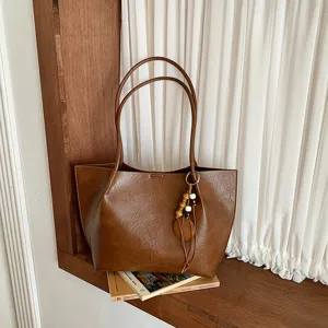 Vista detallada del bolso tote vintage marrón con textura, asas dobles y colgante de cuentas.