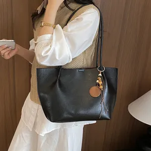 Detalles en primer plano del bolso tote negro de cuero PU con elegante borla colgada.