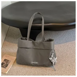 Dettaglio borsa shopper in tela grigio scuro con tracolla ciondolo stella e logo stampato.