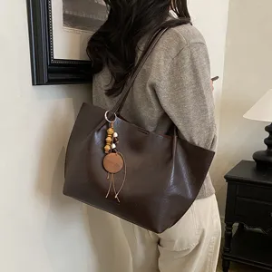 Vista detallada del bolso tote marrón vintage de cuero con colgante de cuentas de madera puesto.