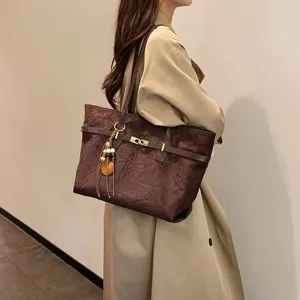 Detail view of the elegant brown shoulder tote bag featuring a metal buckle and tassel pendant.