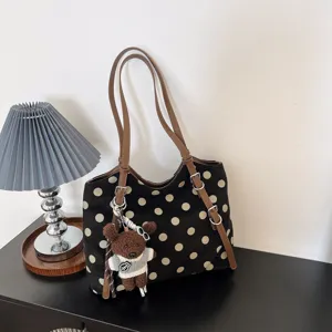 Detalle de bolso tote con lunares negros, asas marrones y un adorable colgante de osito.