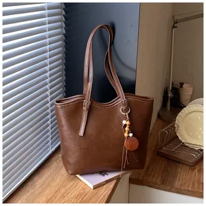 Vista detallada del bolso tote de cuero marrón con textura, doble asa y bonito colgante.