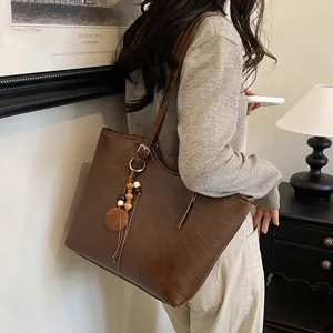 Vista detallada del elegante bolso de hombro de cuero marrón con colgante de borla decorativa.