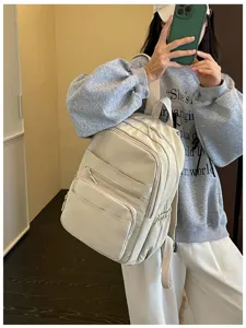 Detailed view of the casual multi-pocket beige backpack worn by a model in lifestyle setting.