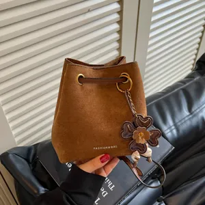 Detailansicht der braunen Wildleder Eimer Tasche mit süßem Blumenanhänger und Kordel.